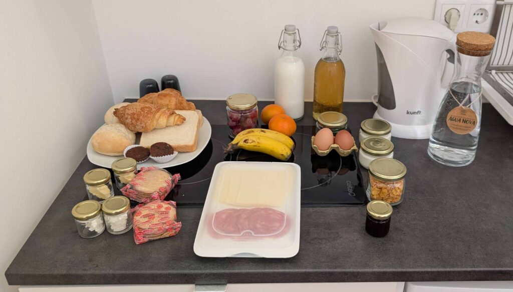 A large breakfast spread.  There are a variety of breads, fruits, eggs, and condiments.  Glass jars for things like butter and salt.  A couple of glass bottles for milk, juice, and water.