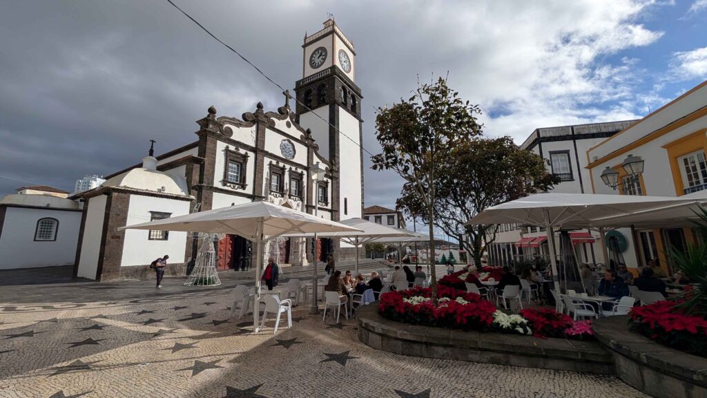 A photograph of Ponta Delgada featuring a coffee shop named Cafe Central. A large white church is in the background.