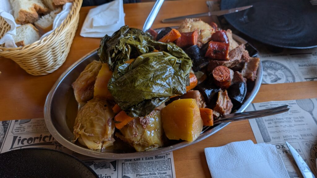 A plate filled with chorizo and blood sausage, chicken, pork and beef, two kinds of potato plus yams, two kinds of cabbage, and carrots