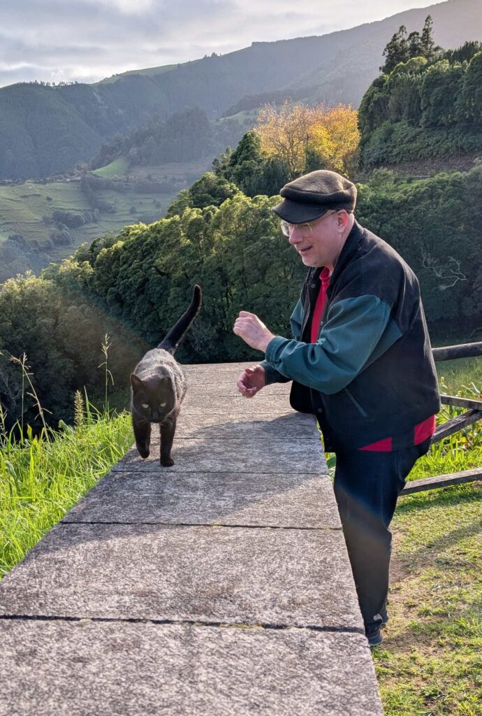 A black cat trotting along a stone fence past the author's spouse.
