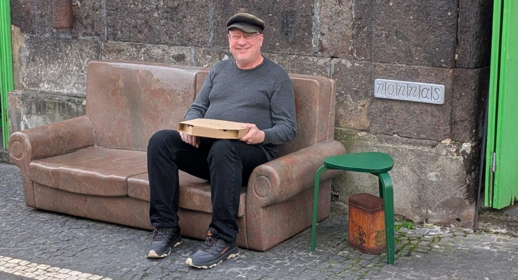 The author's spouse holding a small pizza box while sitting on a stone bench carved to look like a comfortable loveseat.
