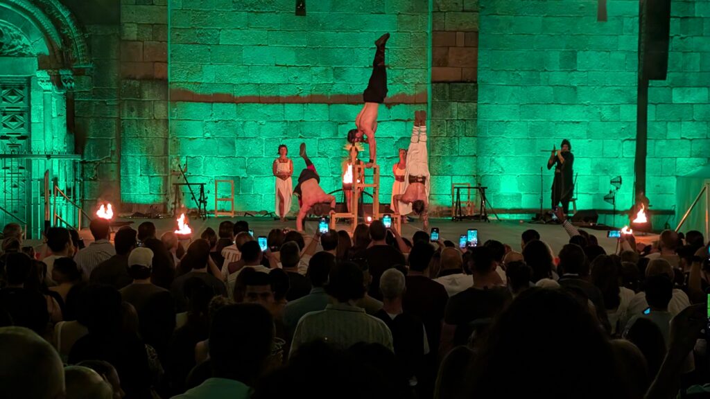 Three acrobats doing handstands, one on several wooden supports balanced together.